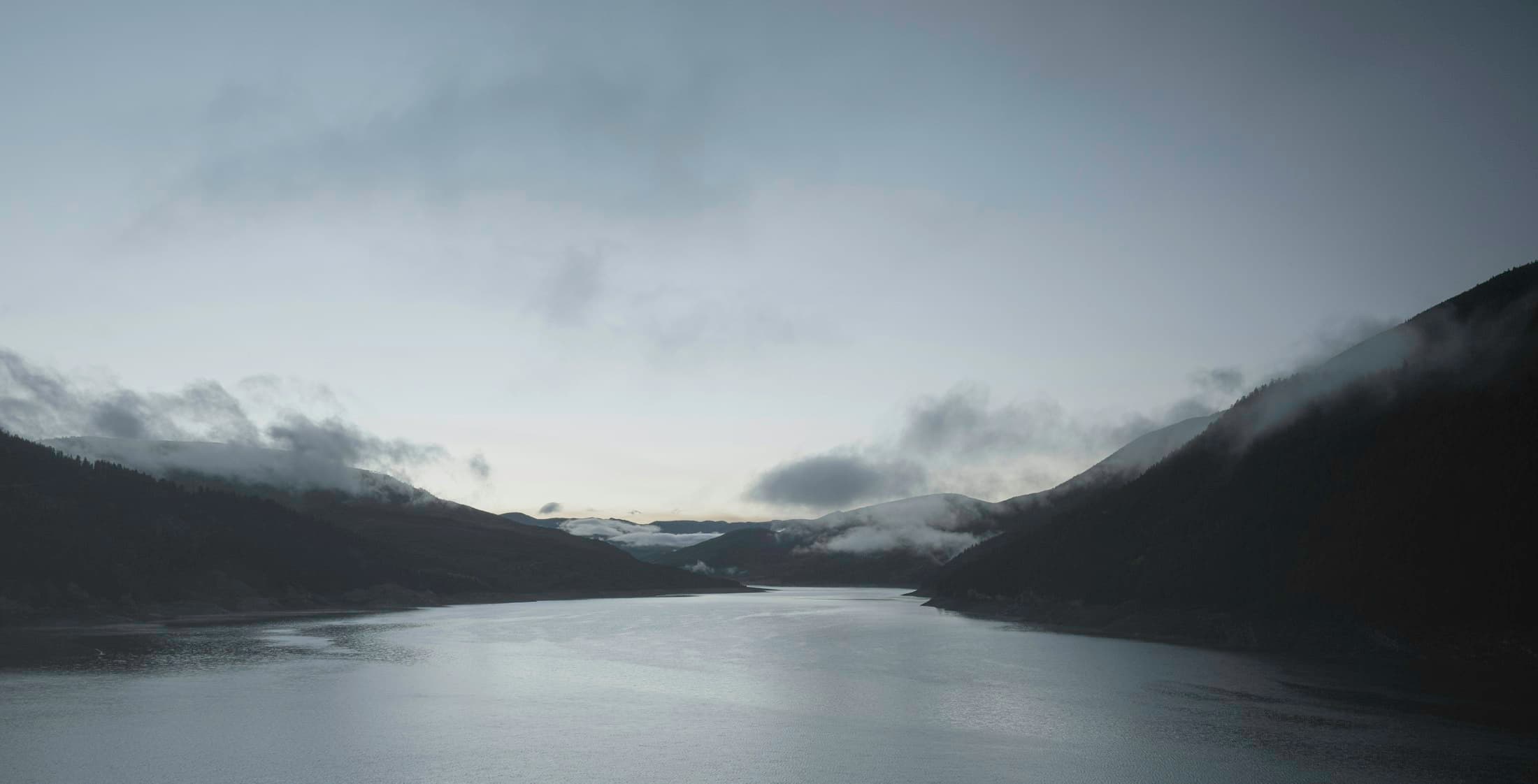 Nebel über einem See zwischen Bergen in der Morgendämmerung